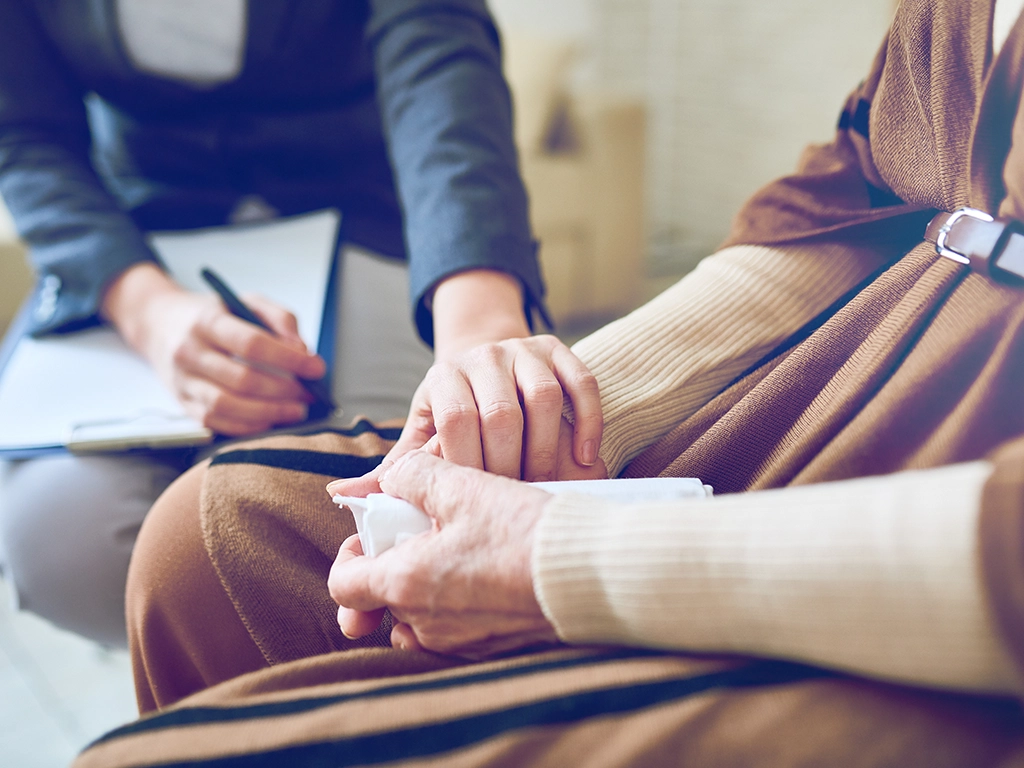 Caregiver holds elderly person’s hand in a comforting, supportive moment during a consultation.