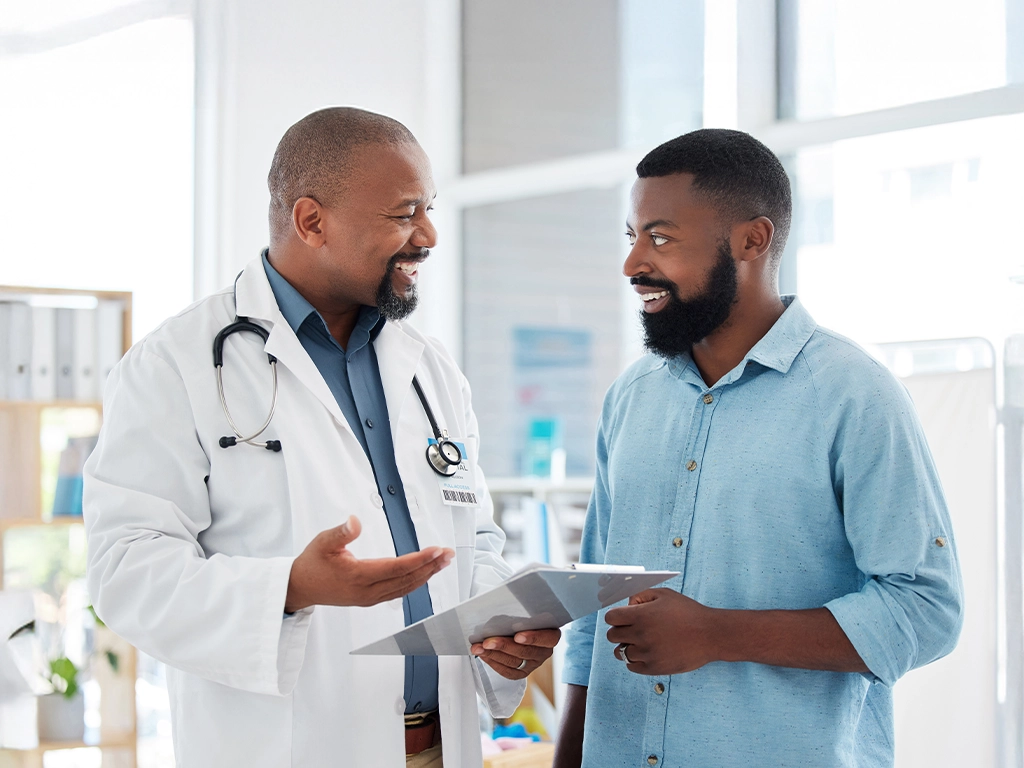 Doctor with stethoscope showing a tablet to a smiling patient in a bright clinic setting.